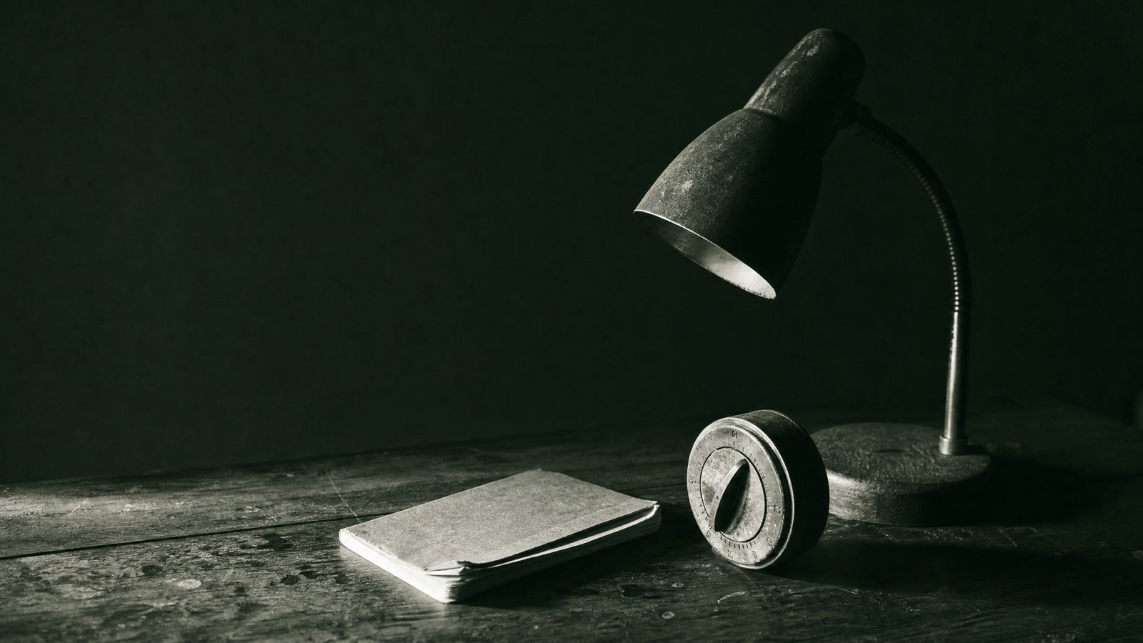 A dim room lit by a single monitor, controller resting on a stack of handwritten notebooks