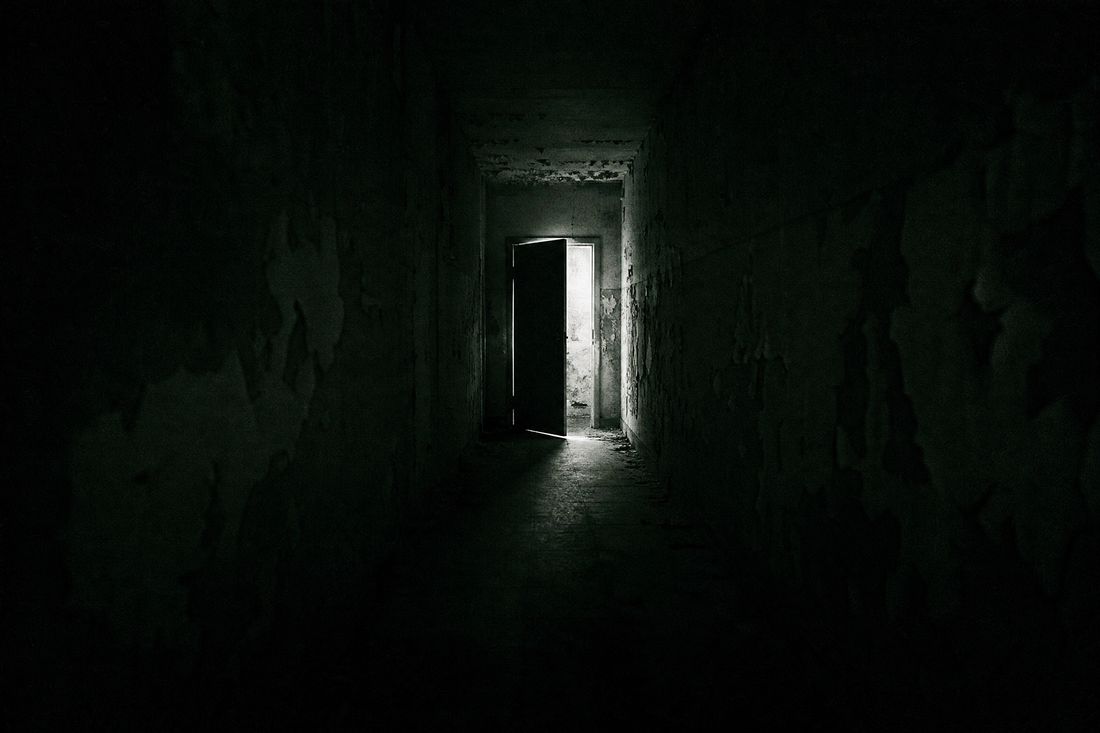 High-contrast corridor lit by a single failing bulb