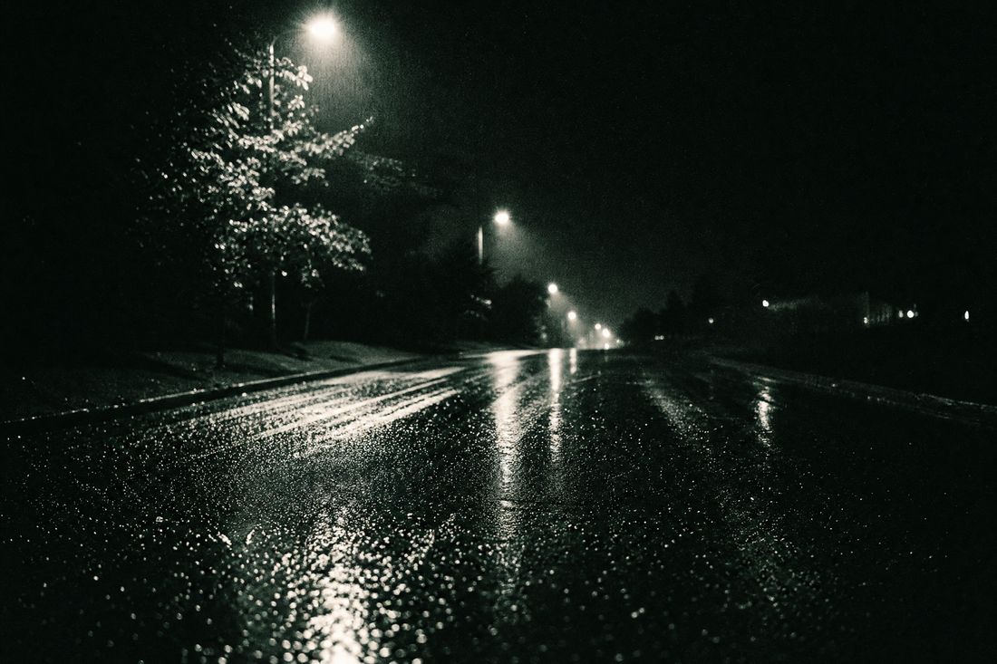 High-contrast image of rain on tarmac with blurred taillights